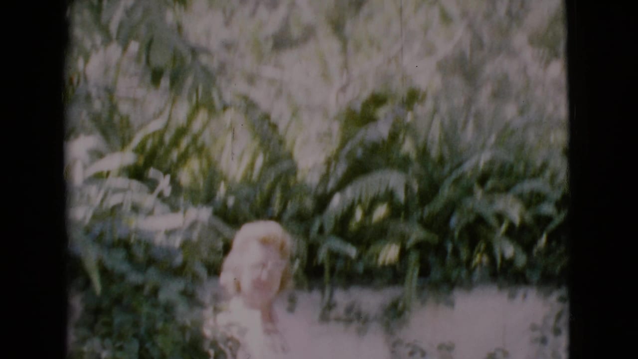 Woman in glasses standing among dense garden foliage.