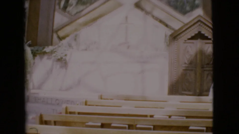 1968 San Diego County church interior showing pews, a pale altar wall with a cross, and carved wooden doors.