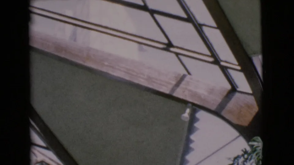 1968 San Diego County 8mm frame with a strong dark vertical mullion, angled glass panes, a wood edge, and shaded wall detail.