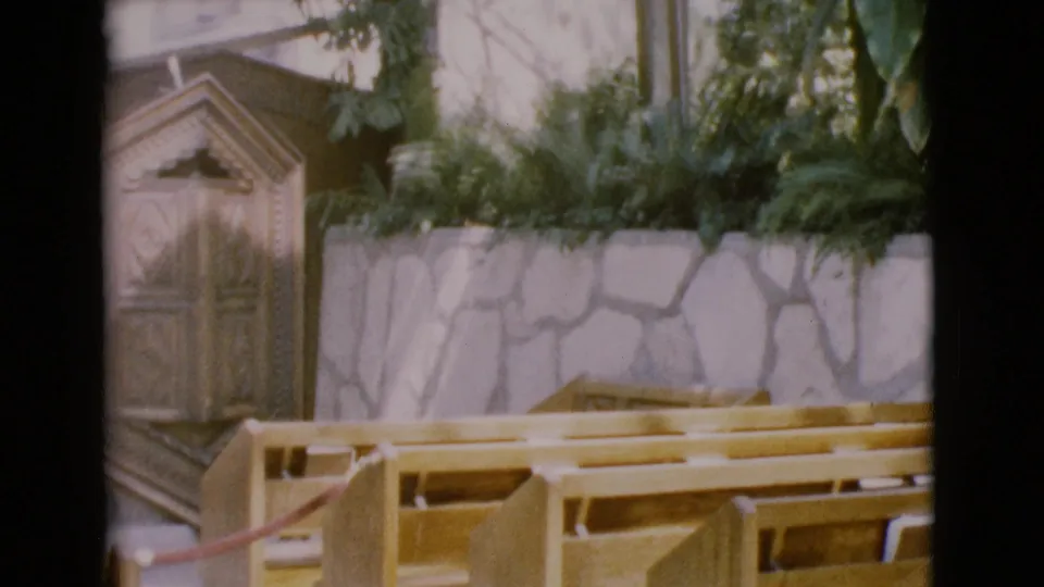 San Diego County 1968 8mm frame showing light wood pews below a planted stone wall in a church setting.