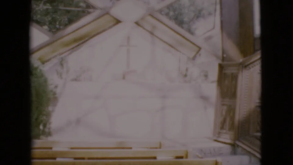 1968 8mm frame of an open-air chapel wall with a simple cross, wooden pews, and a side pulpit.