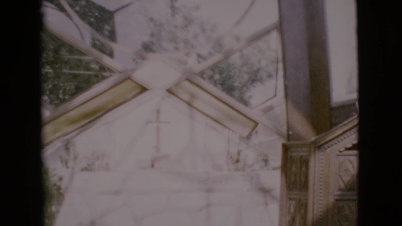 1968 San Diego County home-movie frame looking through stained glass toward a white church facade and cross.