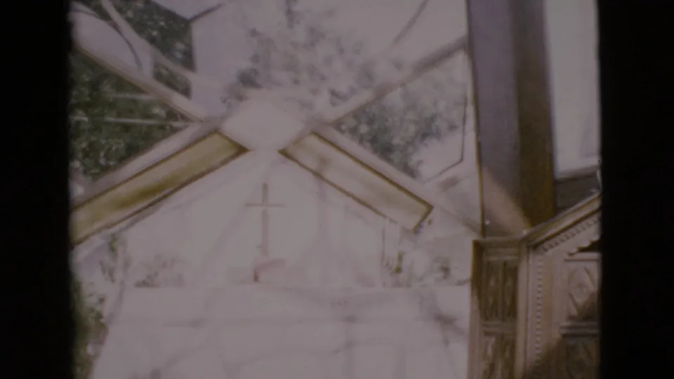 1968 San Diego County home-movie frame looking through stained glass toward a white church facade and cross.