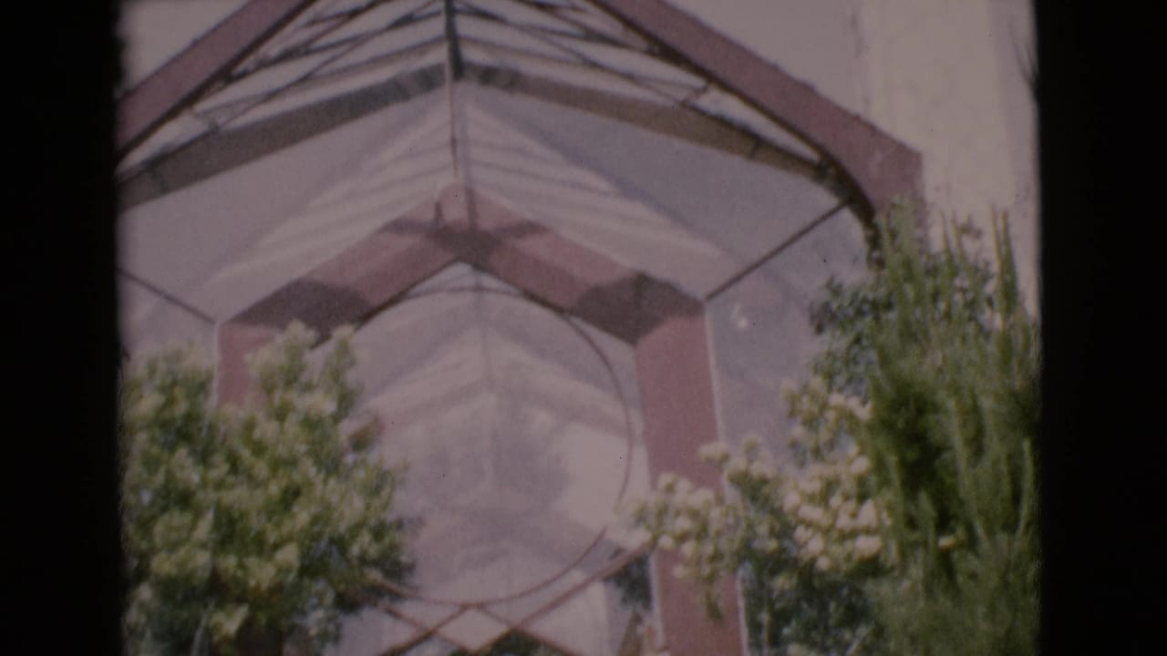 Glass-and-steel archway with trees and shrubs below the entrance structure.