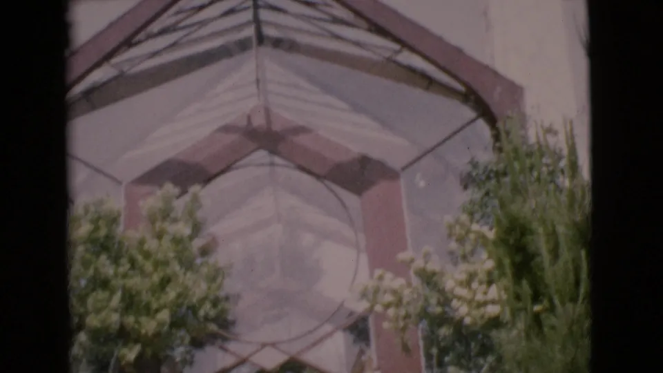 1968 San Diego County home-movie frame of a sunlit glass archway and landscaped building approach.
