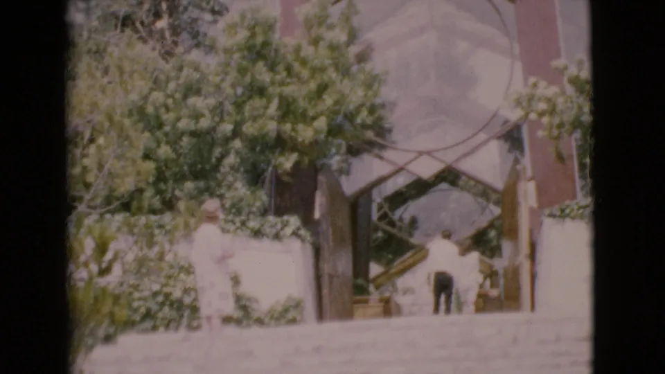 1968 San Diego County 8mm frame with visitors at a landscaped entrance under a large geometric glass arch.