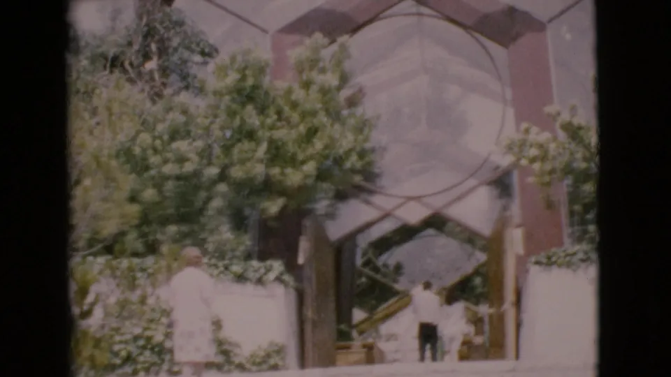 A man descends broad steps while a woman in a light dress stands near greenery outside a modern San Diego County building in 1968.