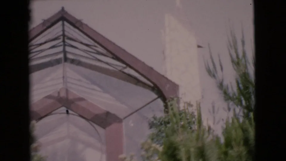 1968 San Diego County 8mm frame showing a white church-like steeple, roofline, dark window edge and green foliage.