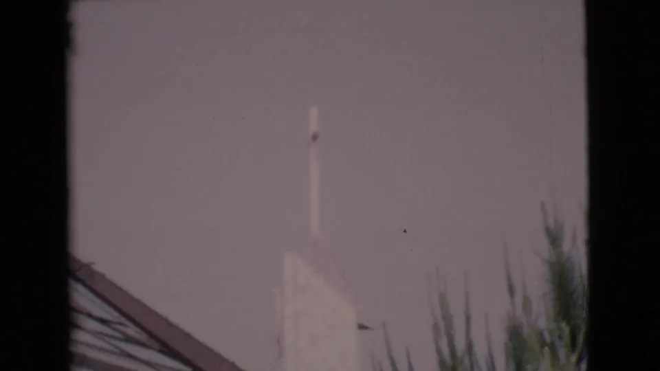 The 1968 home-movie frame shows the white tower rising above roof framing and trees, with muted color and haze.
