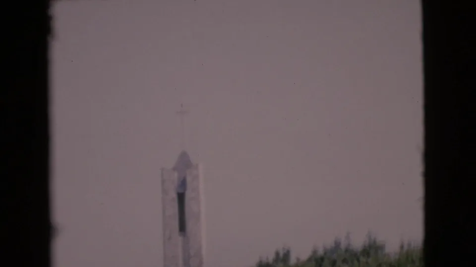 1968 San Diego County 8mm frame showing a distant white church steeple rising above green trees under a muted sky.
