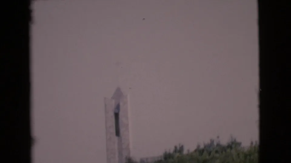 Distant 1968 San Diego County view of a white church steeple above trees, bordered by dark 8mm frame edges.