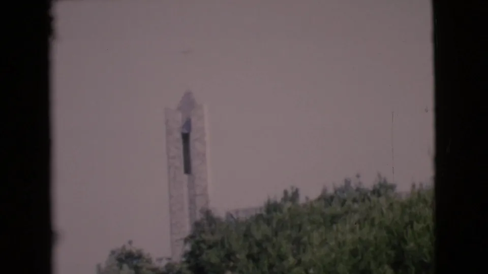 Soft 8mm frame from San Diego County in 1968 showing a church steeple behind green treetops under a pale sky.