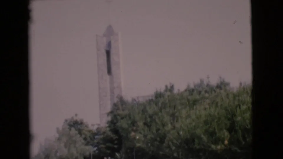 1968 8mm San Diego County view of a white church steeple partly screened by leafy trees and dark frame borders.