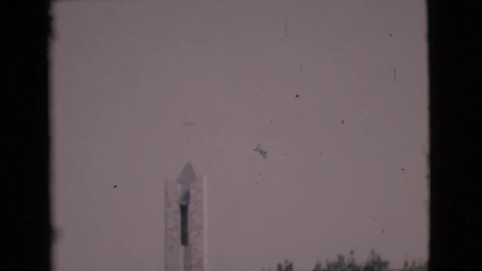 A distant stone chapel tower with a cross is seen against a pale sky in soft 1968 home-movie footage.