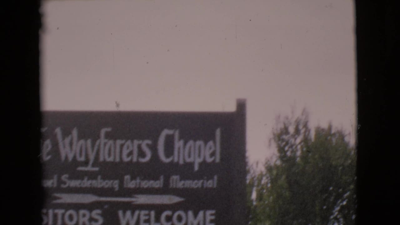 Partial Wayfarers Chapel sign seen beside trees with a vertical film border.