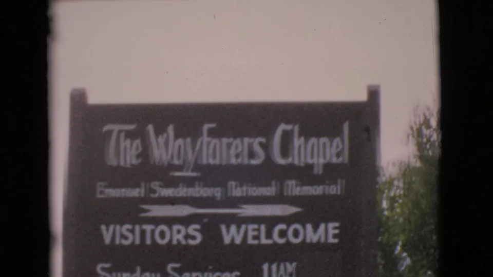 1968 8mm frame showing The Wayfarers Chapel sign, visitor welcome text, and a white arrow pointing along the road.