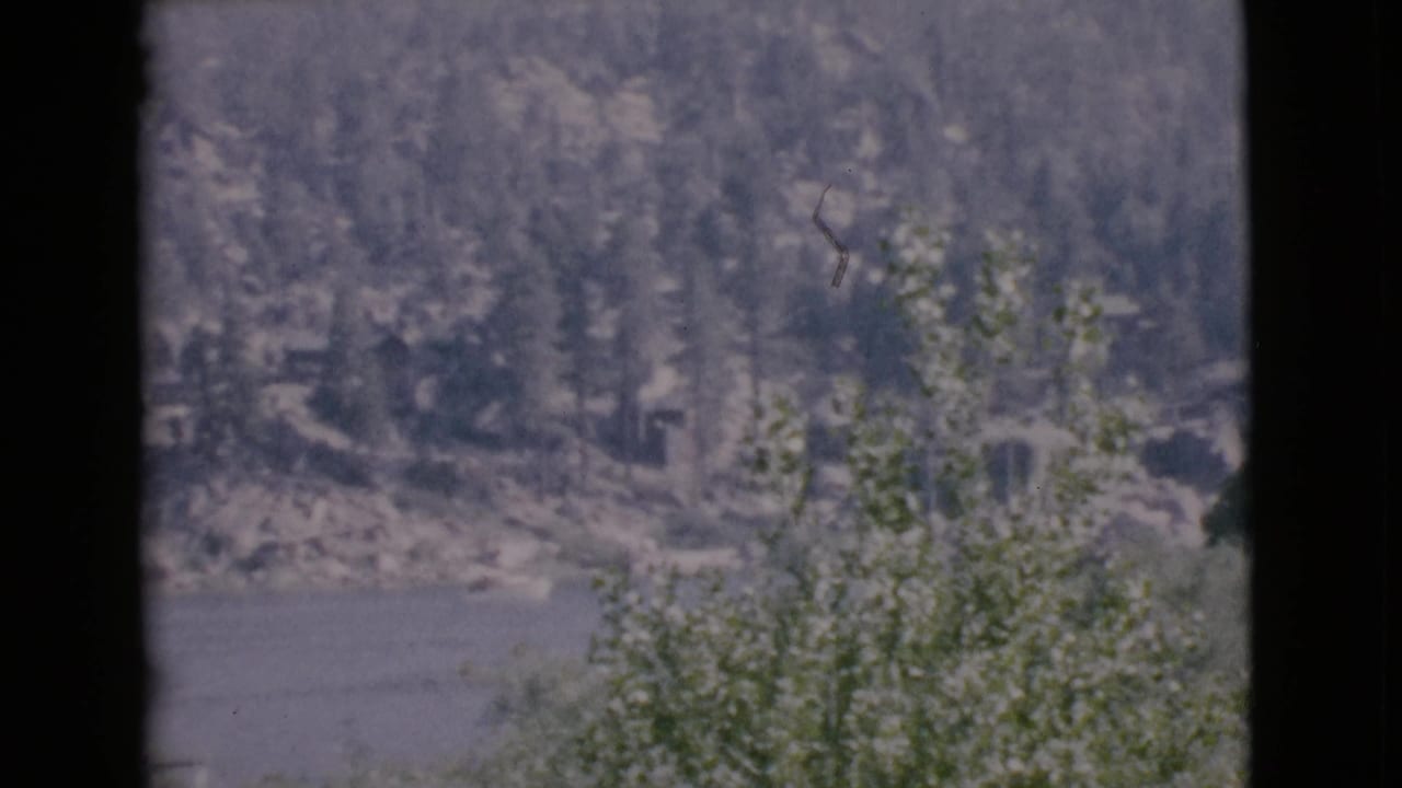 Window-framed view across a lake toward a wooded rocky shoreline.
