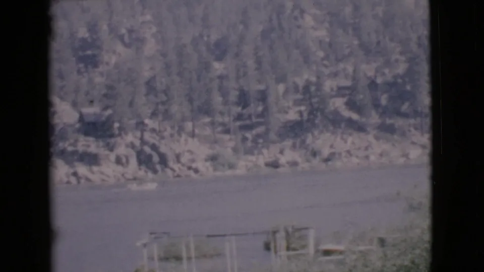 1968 San Diego County frame showing a small boat near the lakeshore, calm water, distant trees, and dark window framing.