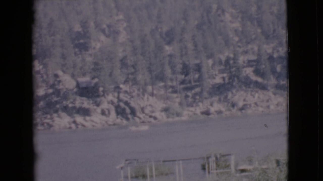 1968 San Diego County lake view with two small boats near the lower frame and a wooded rocky slope in the background.
