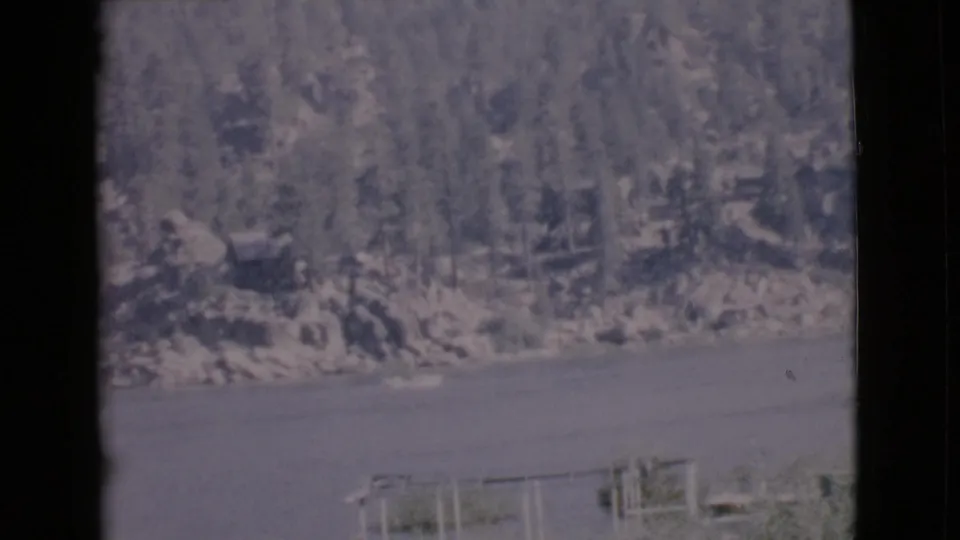 1968 San Diego County lake view with two small boats near the lower frame and a wooded rocky slope in the background.