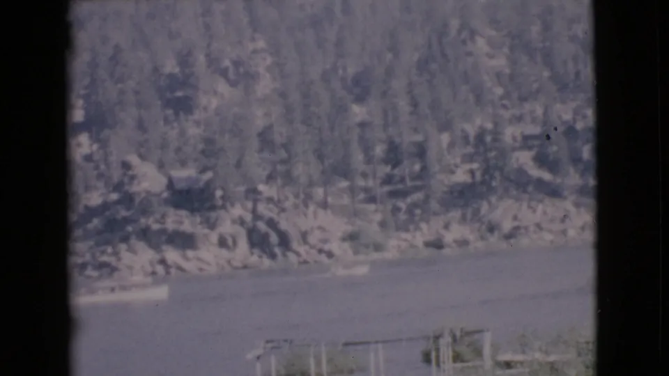 1968 San Diego County home-movie frame showing boats on lake water against a wooded, rocky shoreline.