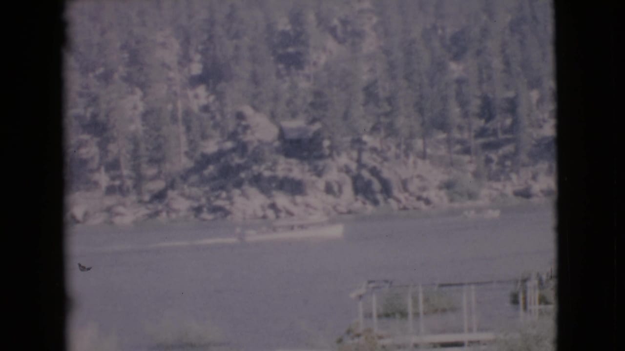 Boat on a lake with wooded hillside and a dock or railing at the lower right.