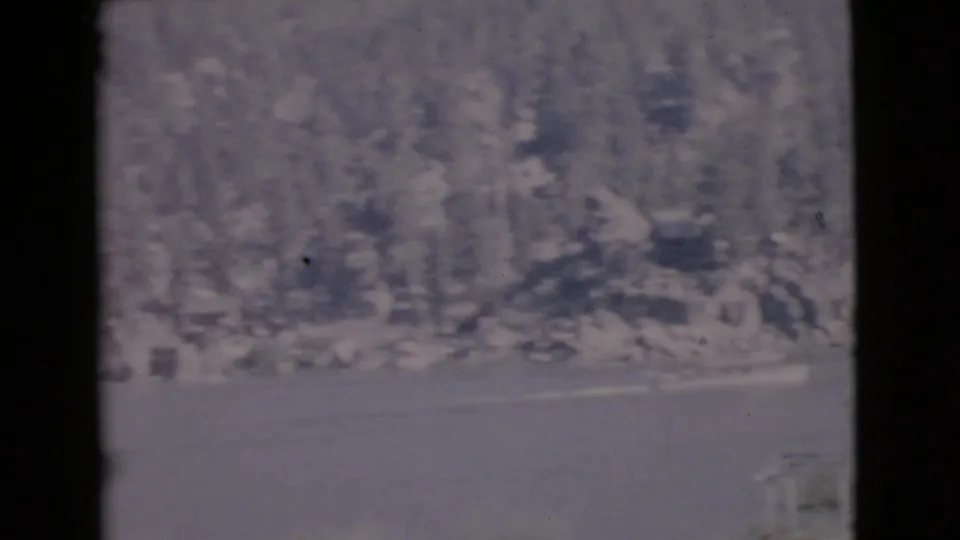 Soft 8mm frame of a San Diego County lake, with wooded shoreline, rocky banks, and a small boat moving across the water.