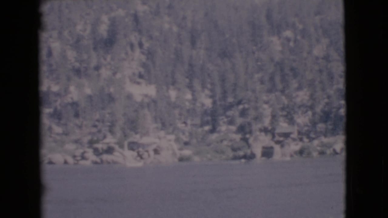 Distant wooded lakeshore across calm water with dark film borders.