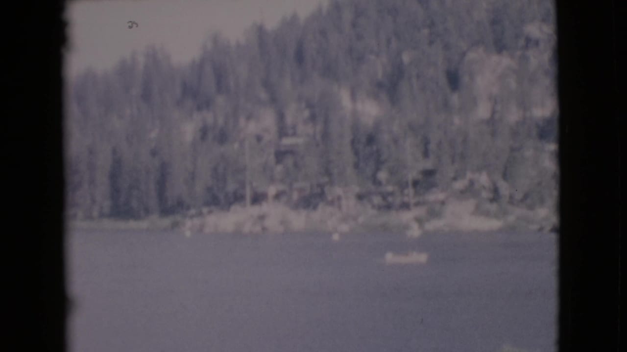 Small boat on a lake with wooded shoreline and dark film gate edges.
