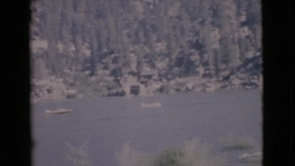San Diego County lake scene on 8mm film, showing small boats near a wooded and rocky shoreline.
