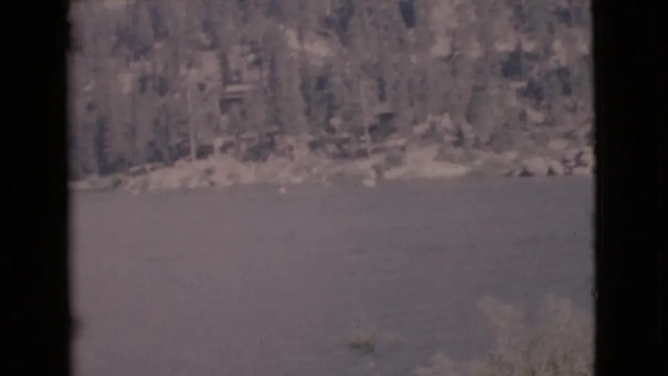 Vintage 8mm frame of a calm lake and tree-lined shore in San Diego County, with dark vertical borders partly obscuring the view.