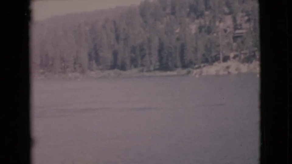 Faded 8mm view of a still lake, forested shore, and faint foreground brush in San Diego County archival home-movie footage.