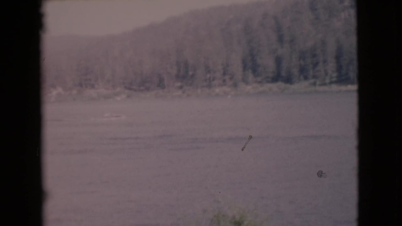 Wide lake view with tree-lined shore, hazy hills, and dark frame border.