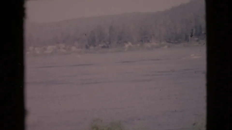 1968 San Diego County 8mm frame of rippled lake water and a distant wooded shoreline, with faded color and visible film wear.