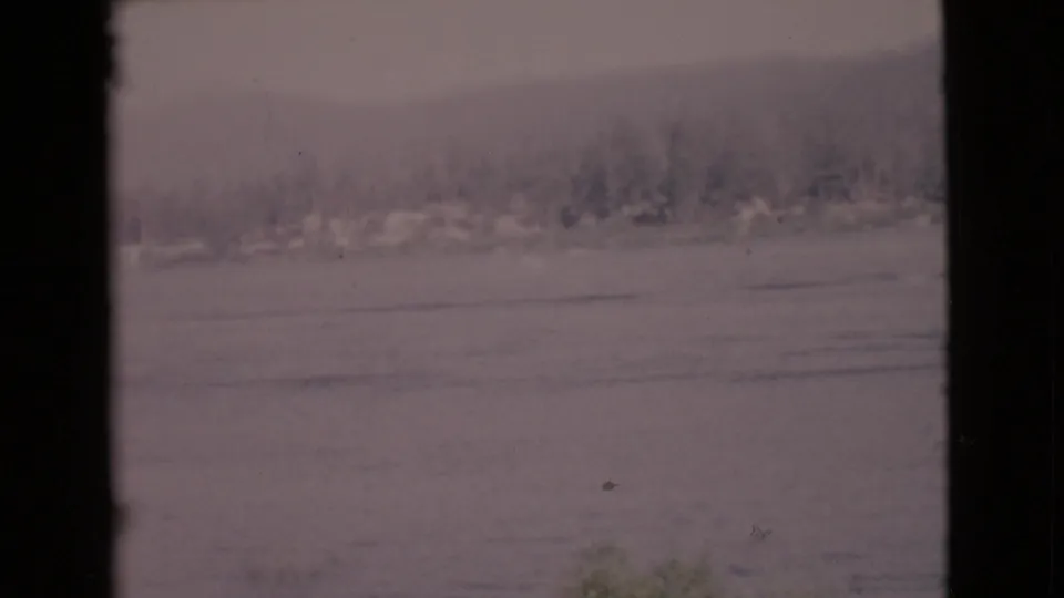 1968 San Diego County home-movie frame showing calm ocean water, distant trees, low hills, and dark foreground frame edges.
