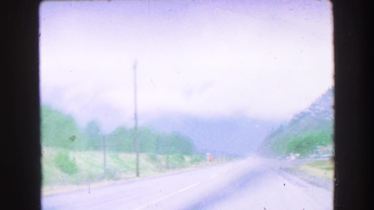 Misty road through a mountain landscape seen from a moving vehicle.