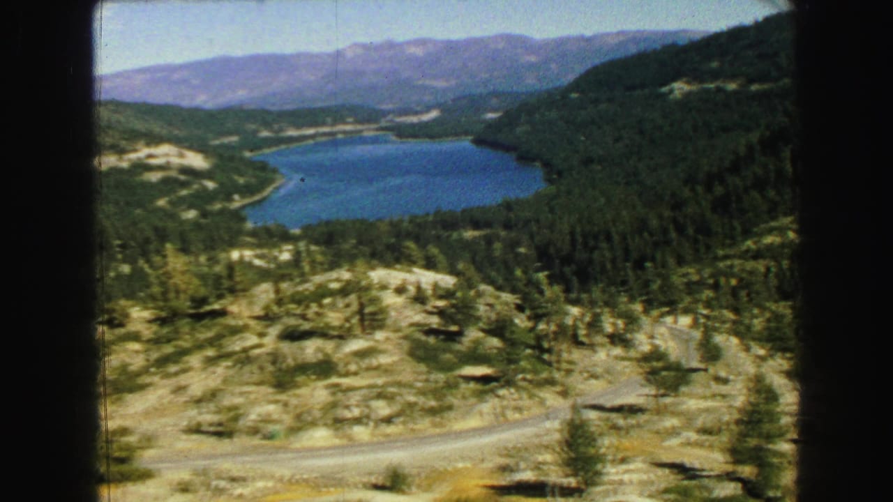 A scenic 1968 Vancouver-area view shows a blue lake among forested hills, distant mountains, and a winding road.