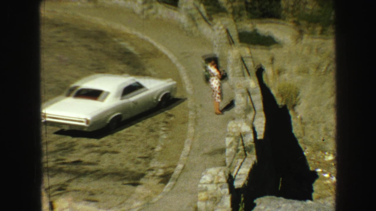 White car beside a curving mountain road near a rocky overlook.