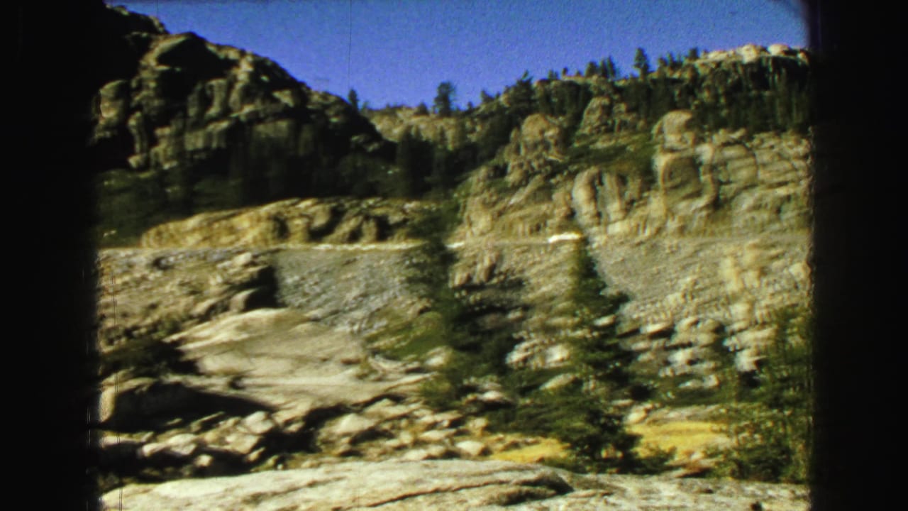 Rocky mountain road cut with evergreen trees under a blue sky.