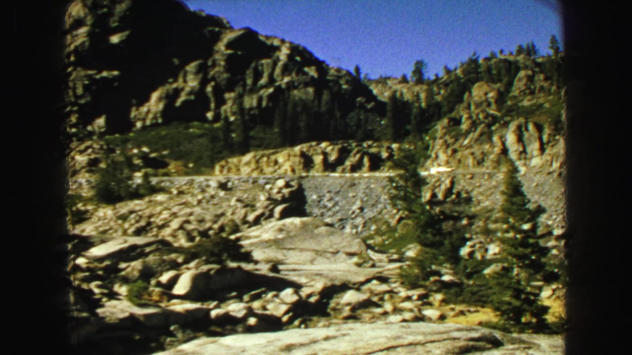 Roadside rock wall, boulders, and trees in a mountain landscape.