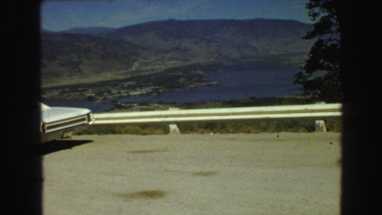 Lake valley view beyond a roadside guardrail with part of a white car visible.