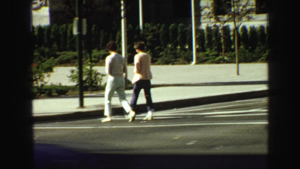 Two pedestrians walk past a landscaped sidewalk in 1968 Vancouver, seen through a dark car-window frame.