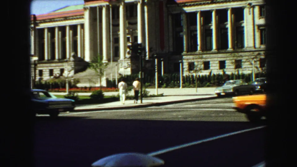 Wide 1968 Vancouver street view with a columned civic-style building, pedestrians, traffic lights, and vintage cars.