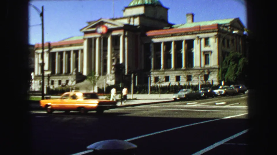 A yellow taxi drives through a 1968 Vancouver street scene with pedestrians and a domed columned building behind it.
