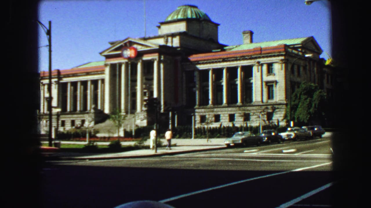 Grand stone building with columns and a dome beside a sunny city street.