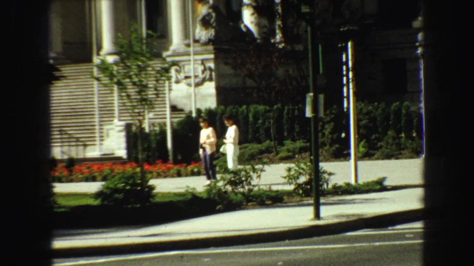 A closer 8mm view shows two pedestrians by red flowers, hedges, and stone steps outside the Vancouver building.