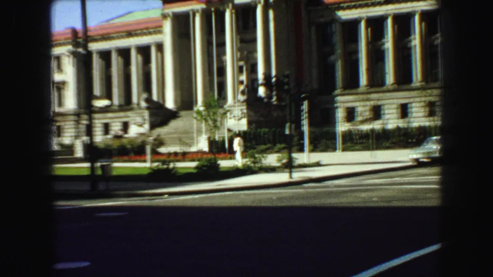 The Vancouver landmark exterior is seen across the road, with columns, lawn, a sidewalk pedestrian, and 1960s street traffic details.