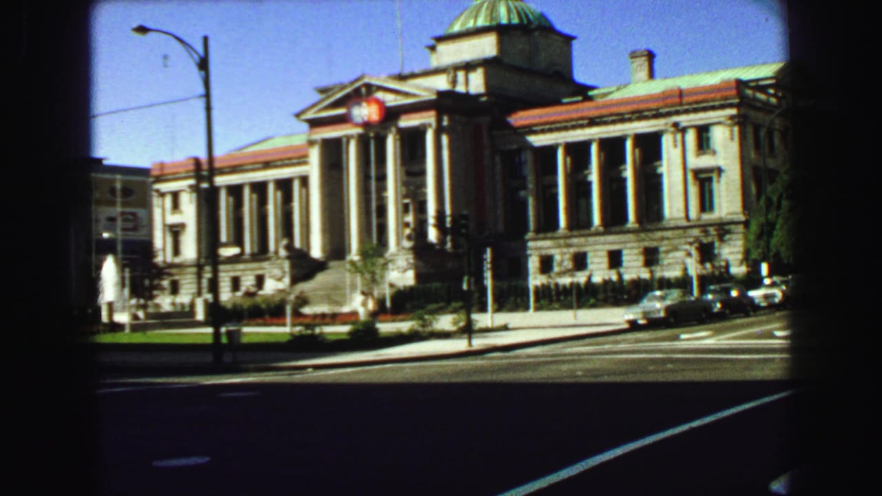 Formal building with columns and a green dome beside a street with cars.