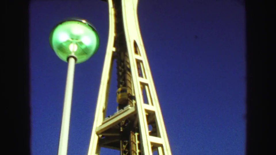 Visitor-shot 8mm frame showing a green lamp pole beside the Space Needle’s white legs and elevator shaft in 1968.