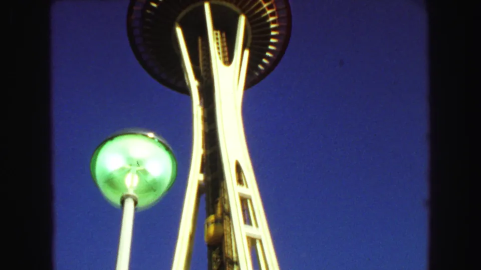 1968 8mm view looking up toward the Space Needle observation deck with a green globe lamp and elevator shaft in the foreground.